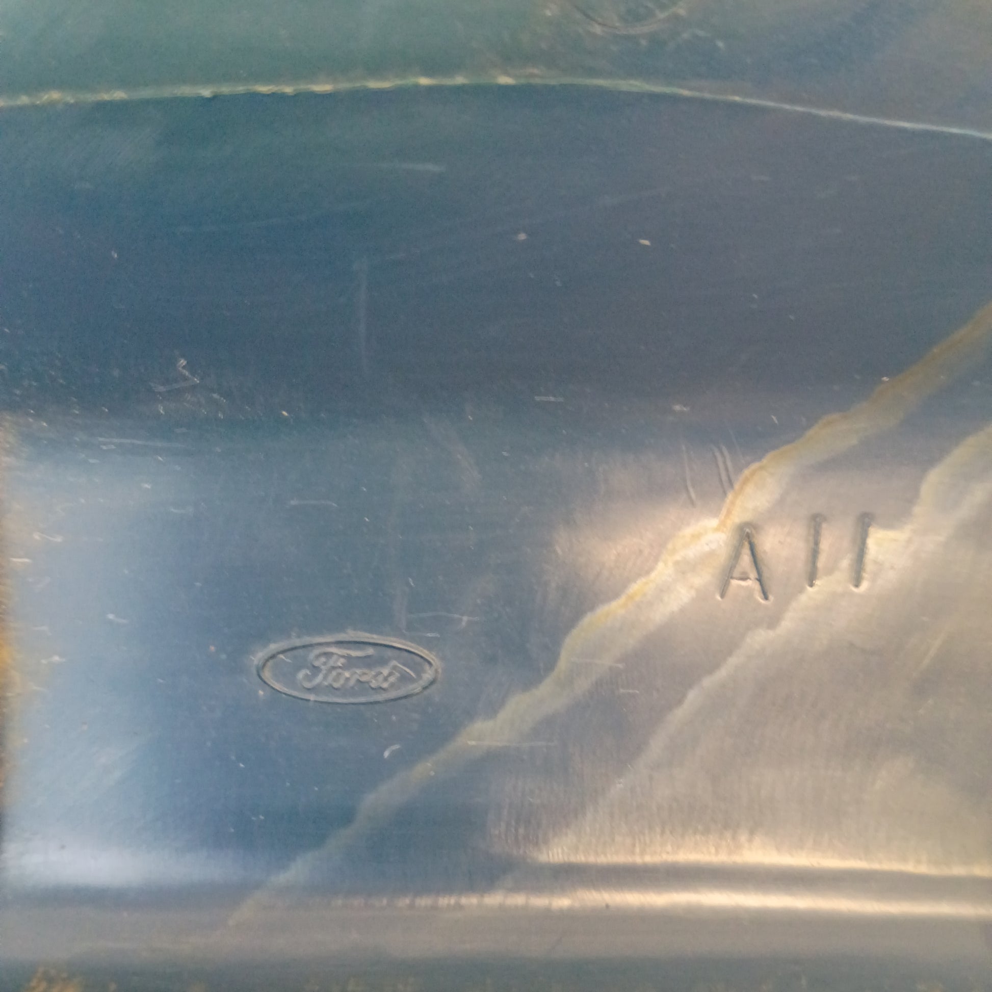 Close-up of a Ford logo embossed on Harbor Blue A-pillar trim from a 1984 Ford F-150, showing scratches and marks.