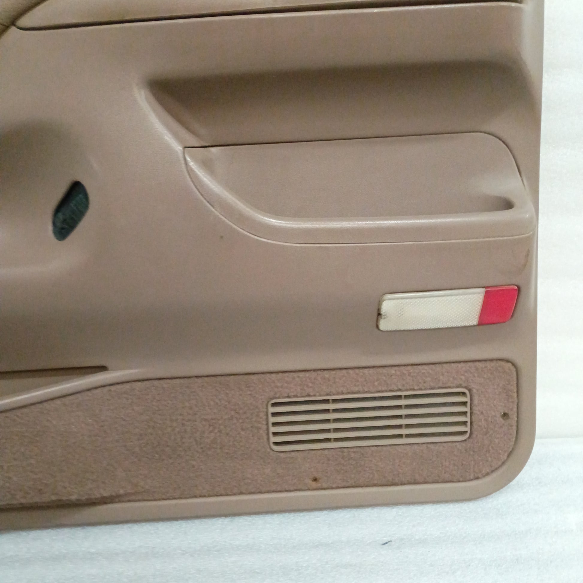 Tan door panel for a Ford truck, featuring a sliver trim, red reflector, speaker grill, and carpeted map pocket.