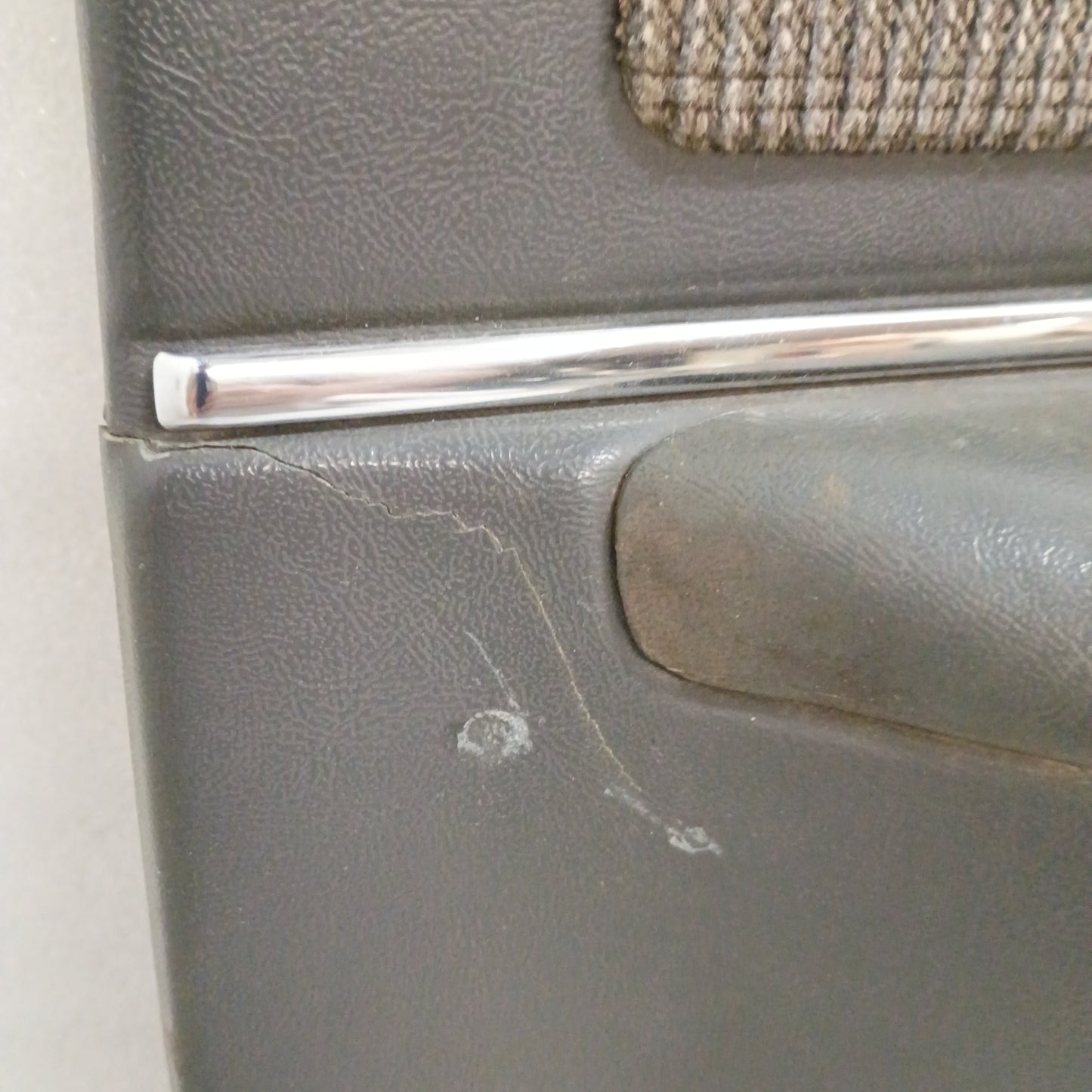 Dark gray Ford door panel with chrome trim and minor crack, featuring textured surface and fabric insert.