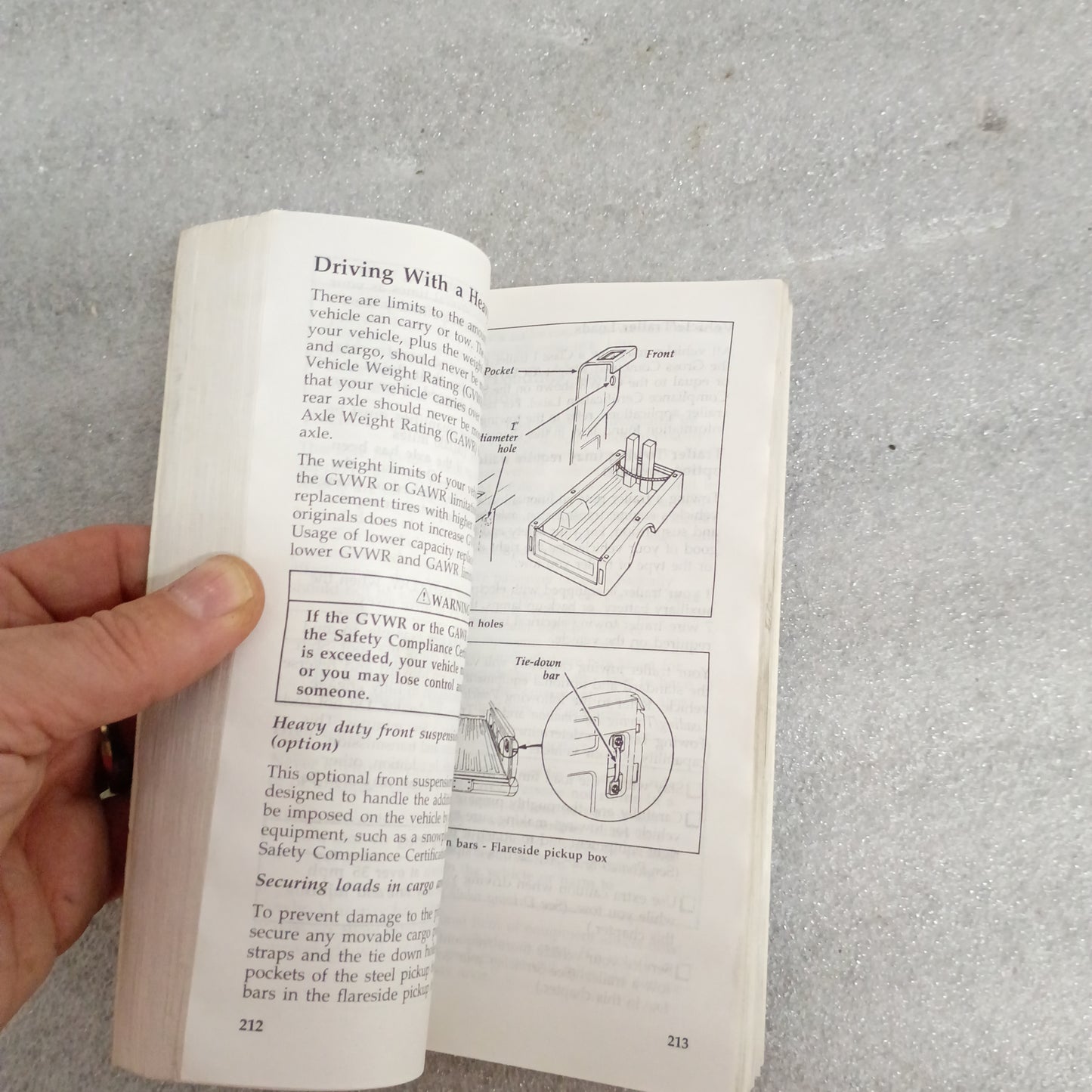Hand holding an open page of a 1996 Ford F-Series Owner Guide, displaying diagrams and text on vehicle weight limits.
