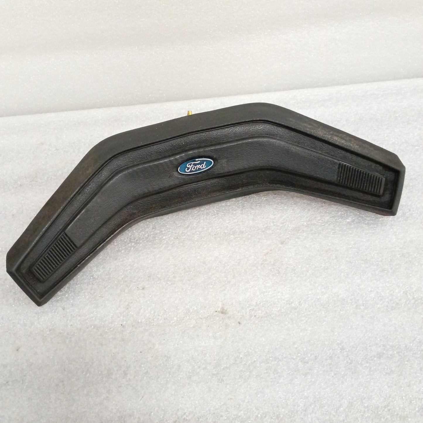 Black Ford OEM steering wheel horn button with central logo, vinyl grain pattern, and worn corners. Fits 80-86 F150, F250, F350, Bronco.