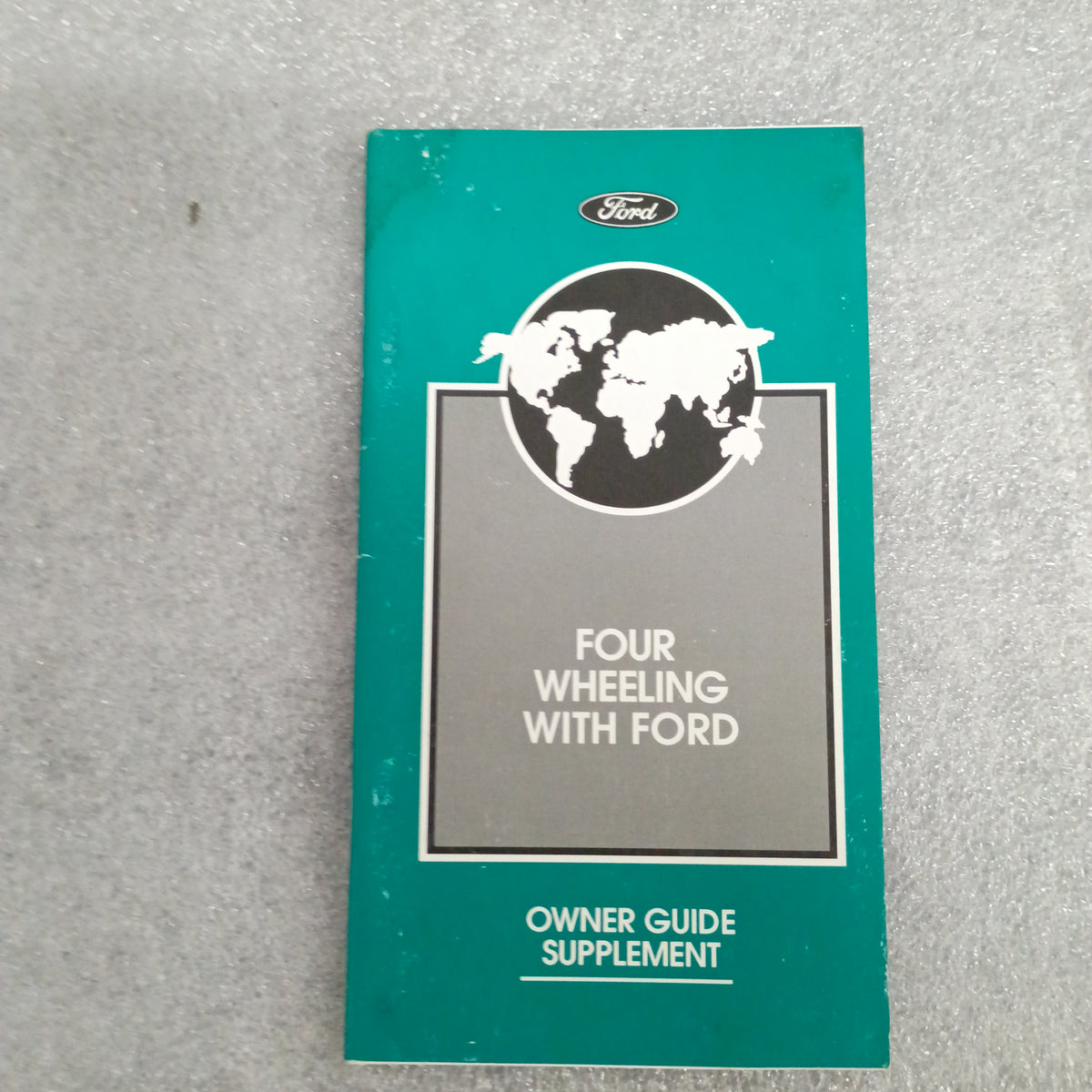 Four Wheeling with Ford Owner Guide Supplement in green cover featuring a world map and Ford logo on a textured surface.