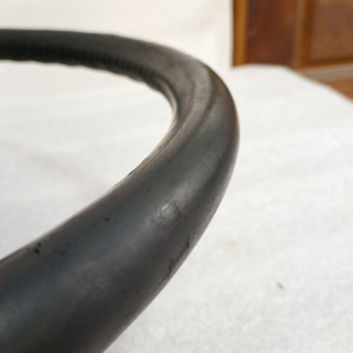 Close-up of a black leather steering wheel edge, showing stitching detail and glossy finish in excellent condition.