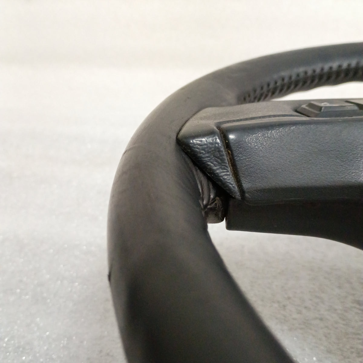 Close-up of a black leather steering wheel with cruise control buttons, compatible with 1987-1991 Ford models, in excellent condition.