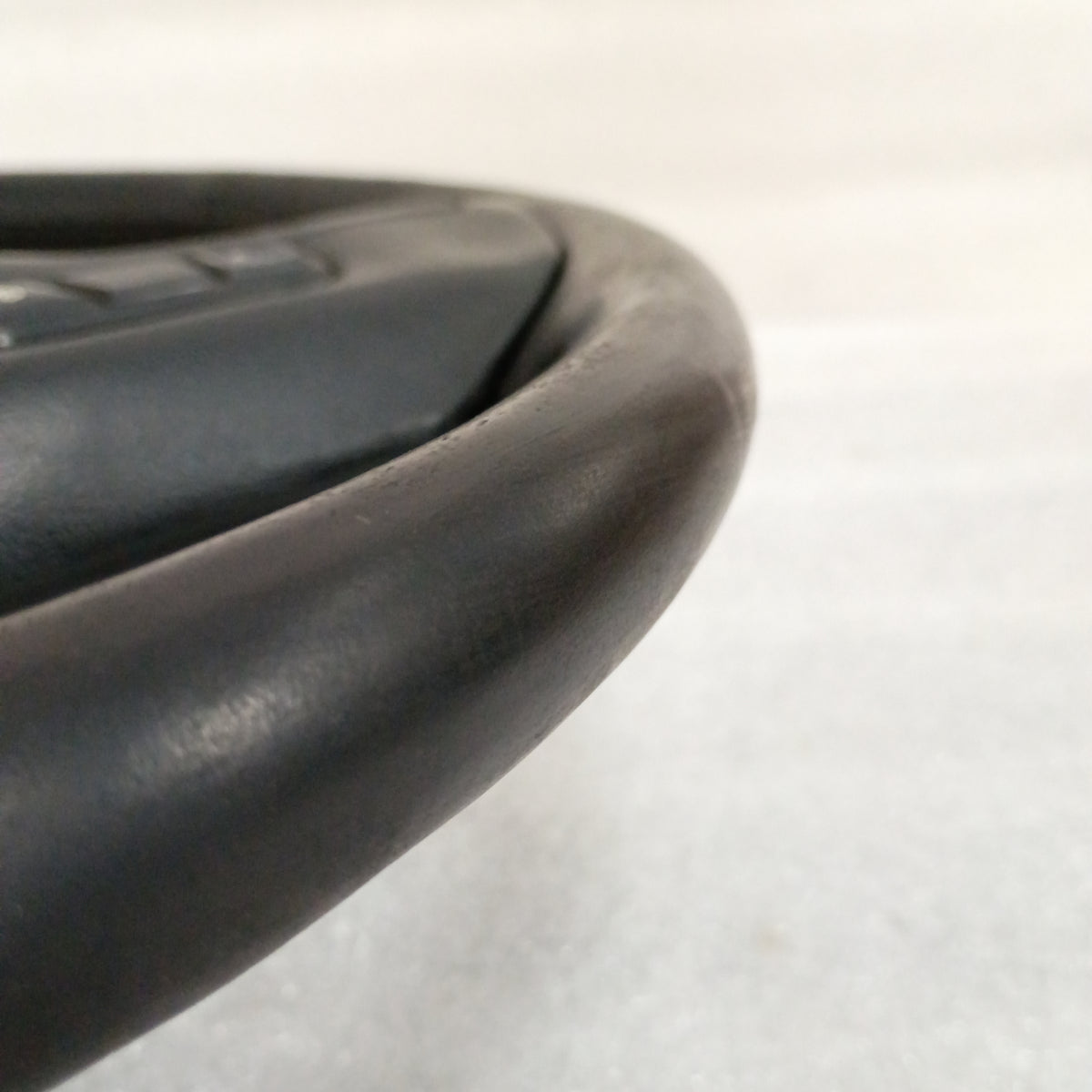 Close-up of a black leather steering wheel edge with horn and cruise control buttons, showing glossy, well-preserved finish.