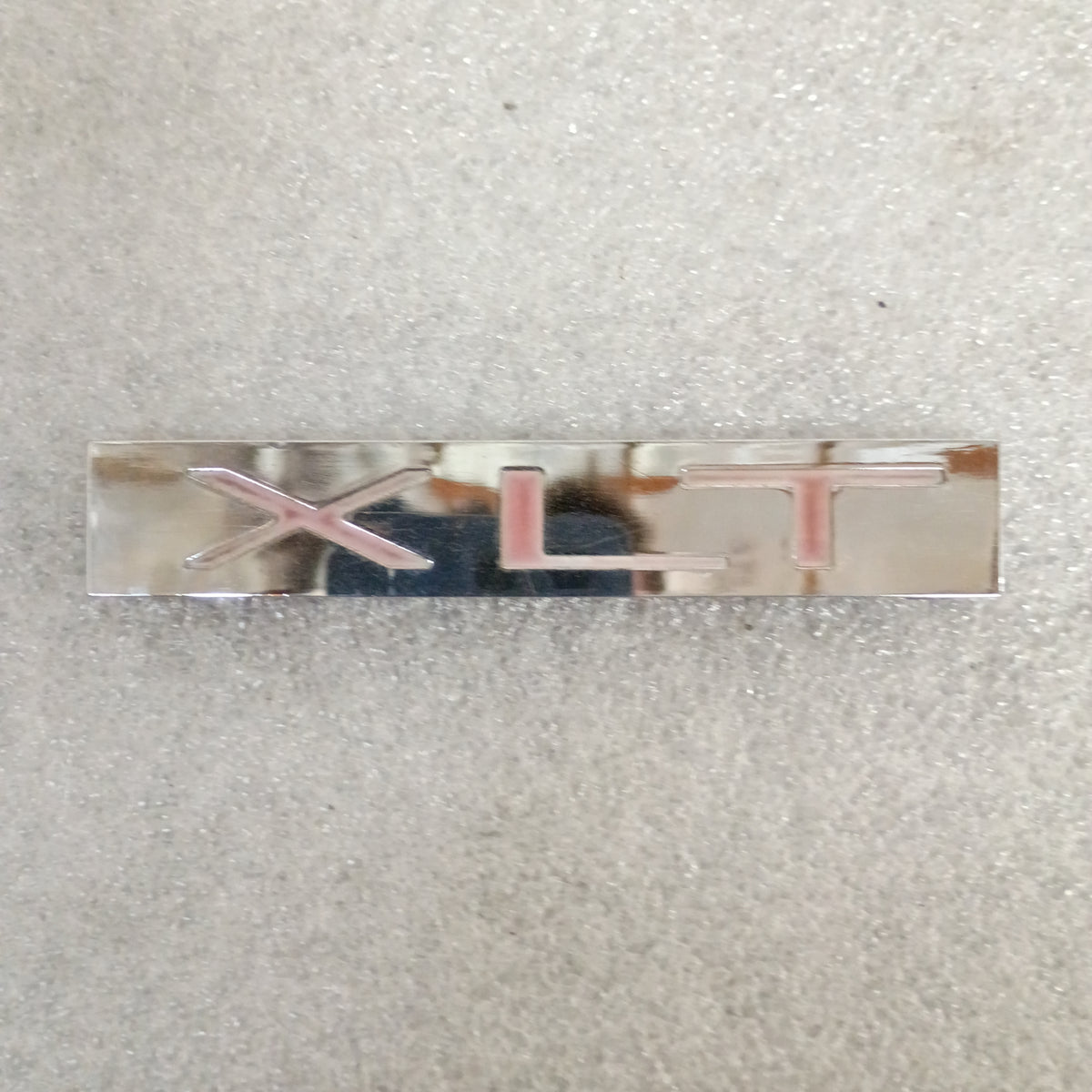 Silver XLT emblem badge from a Ford OEM fender and tailgate set, displaying minimal wear, for 1983-1991 Ford trucks.