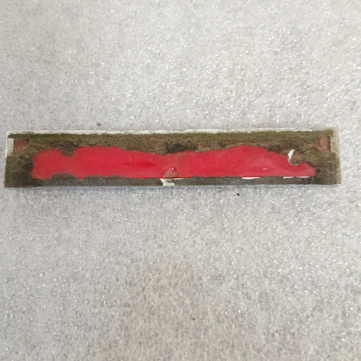 Backside of a worn Ford XLT Diesel emblem from 1983-1991 F-Series trucks, showing red adhesive residue and missing mounting nipples.