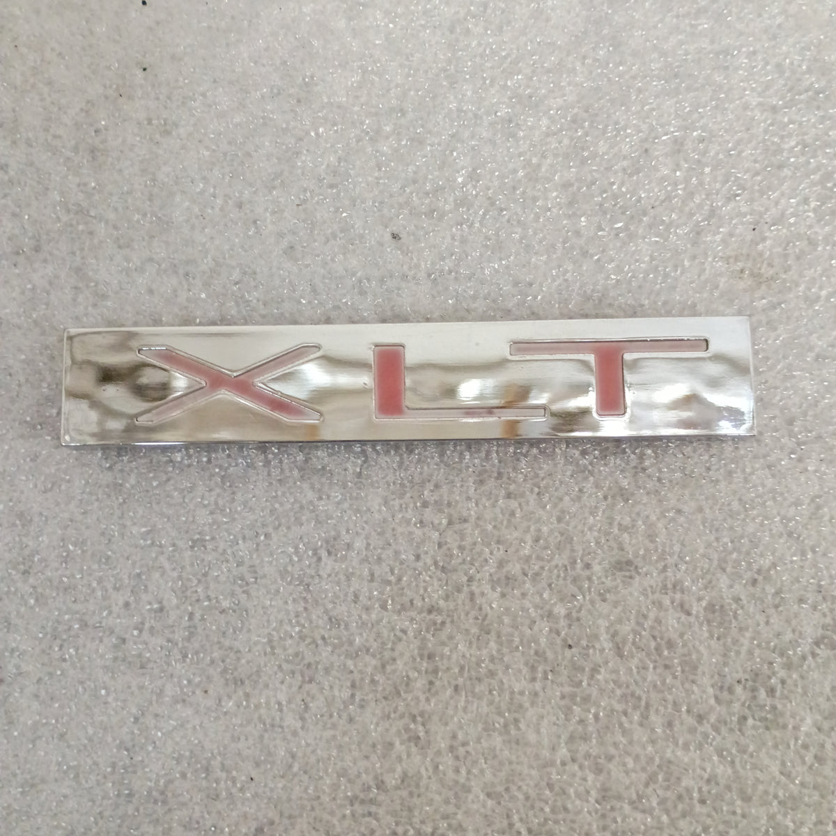 Chrome "XLT" emblem badge for Ford trucks, compatible with 1983-1991 F150, F250, F350, Bronco. Shows normal wear.