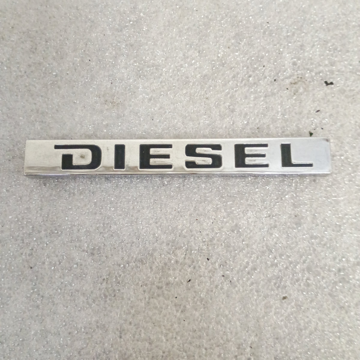 Ford OEM metal "Diesel" emblem, compatible with 1983-1991 F150, F250, F350, Bronco; shows some age wear, no cracks.