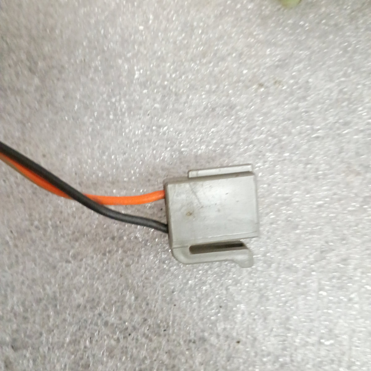 Gray electrical connector with black and orange wires on a textured surface, part of a Ford wire harness for power doors.