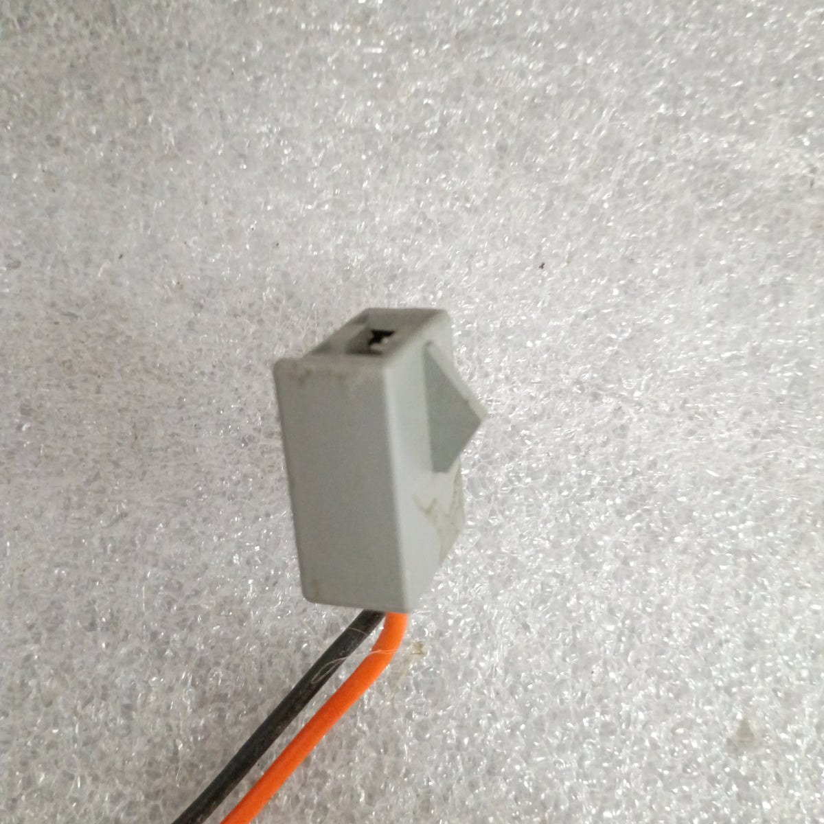 Gray connector with orange and black wires on a textured surface, part of a Ford power window and lock harness set.