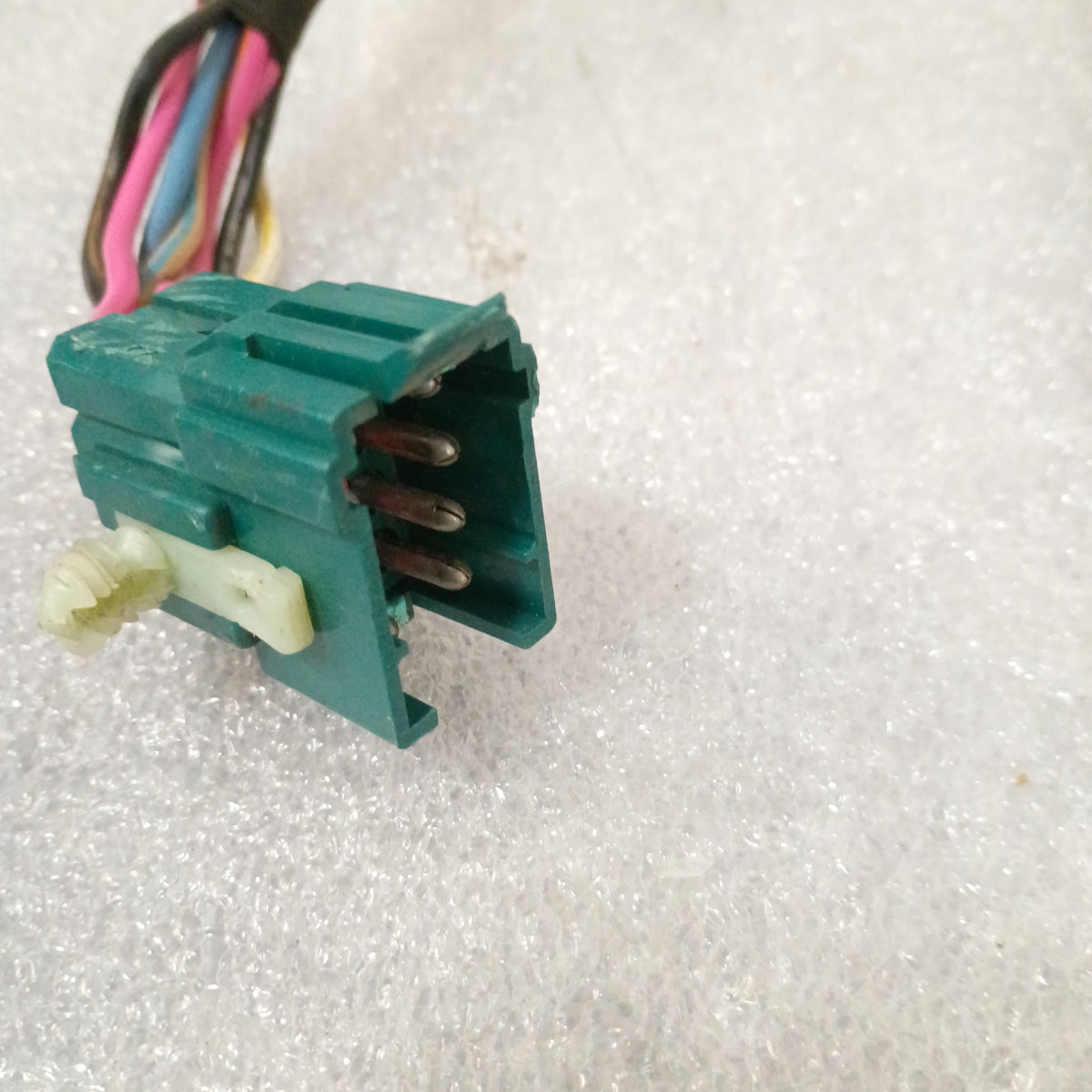 Teal connector with colorful wires for Ford 87-91 power window and lock harness, shown on a textured surface.