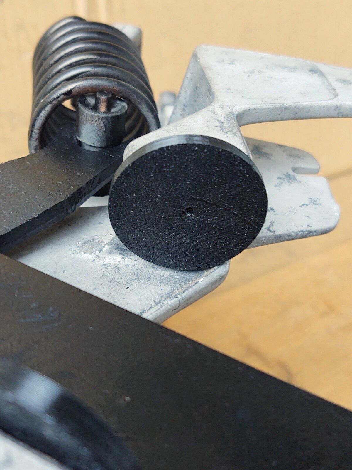 Black circular rubber clutch pedal bumper installed on a silver metal bracket, shown next to a coil spring on a 1980-1991 Ford truck pedal assembly.