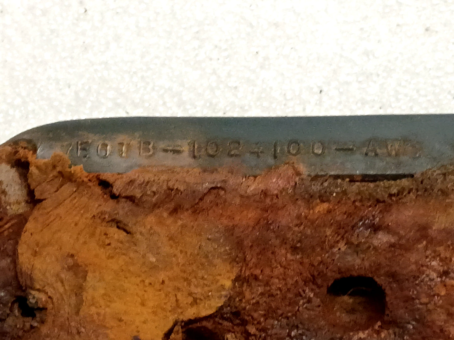 Close-up of a rusted surface with visible Ford part number "E0TB-1024100-AWC" for Dark Harbor Blue arm rests, 1980-1986 Ford models.