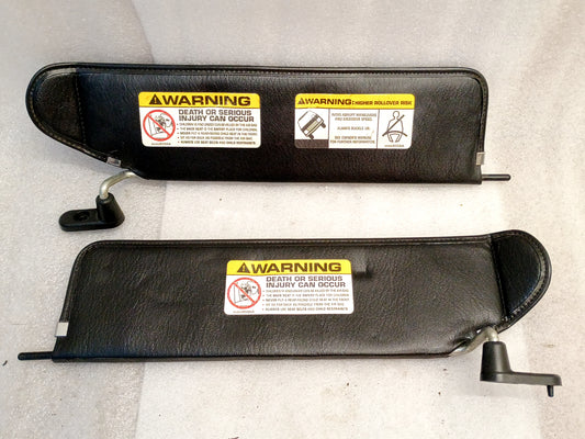 Black sun visors pair for Jeep Wrangler TJ (2003-2006), includes chrome swivels and holder pins, with warning labels visible.