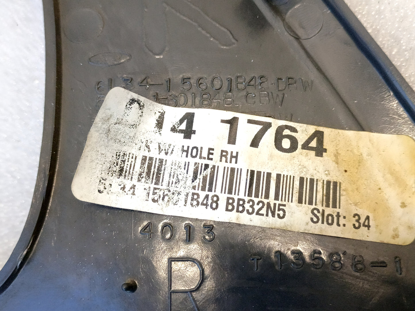 Close-up of a Ford speaker grill cover with part number 5L34-15601B48. Dark gray surface with a barcode label.
