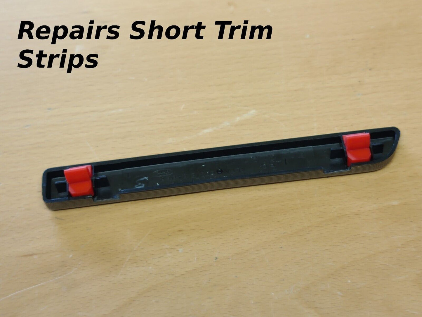 Backside of a short black dash trim strip showing two red repair clips installed at each end, with text overlay reading Repairs Short Trim Strips.