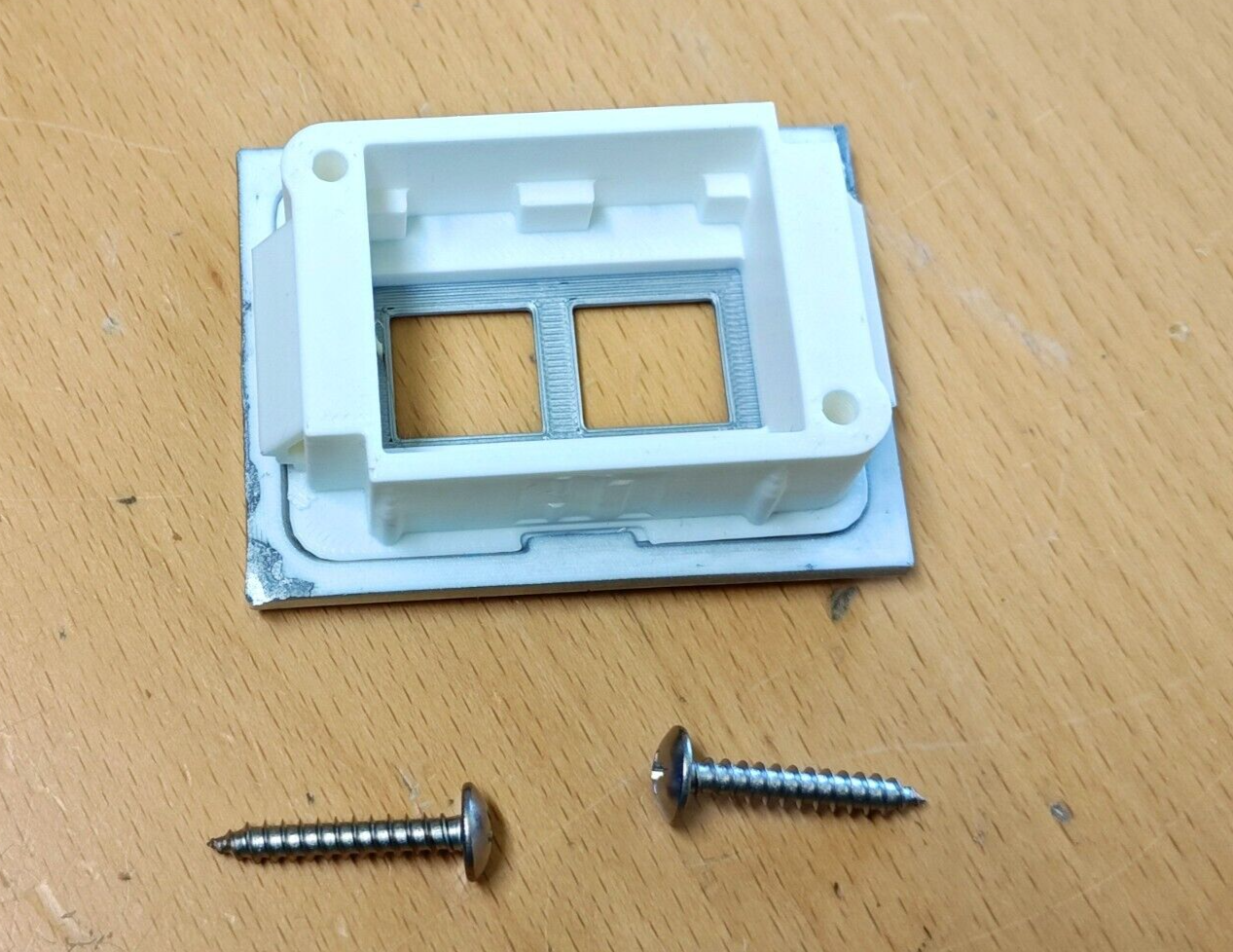 Back view of a white dual power window switch bezel with a silver frame, shown with two included stainless steel mounting screws for 1980-1986 Ford trucks and Broncos.