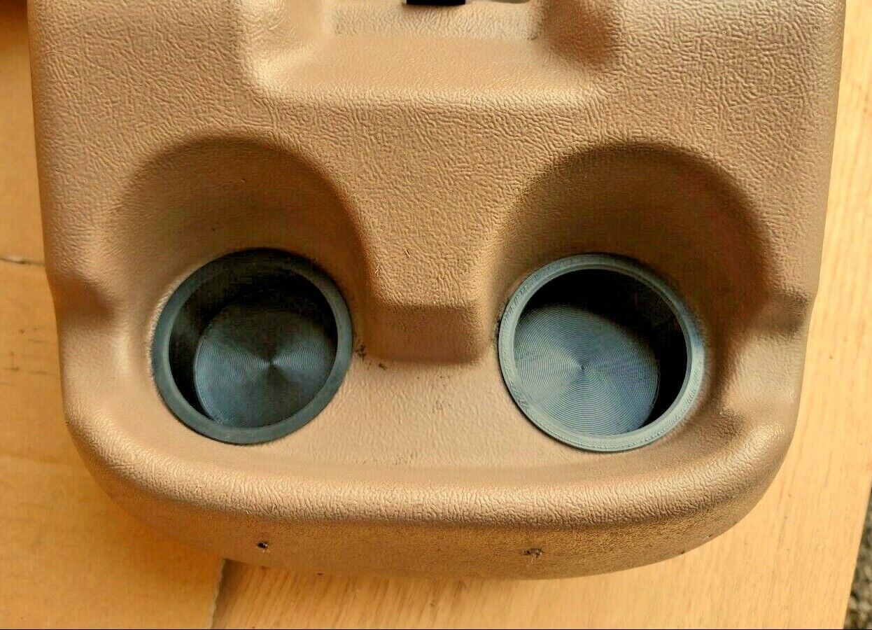 Close-up of two black cup holder inserts installed in a tan textured center console for a 1992-1996 Ford truck or Bronco.