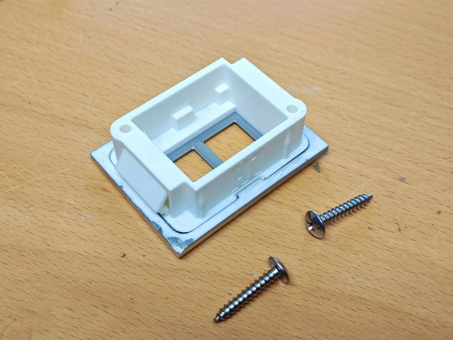 Underside of a white and chrome left power window switch bezel with two stainless steel mounting screws, compatible with 1980-1986 Ford F-Series trucks and Broncos.