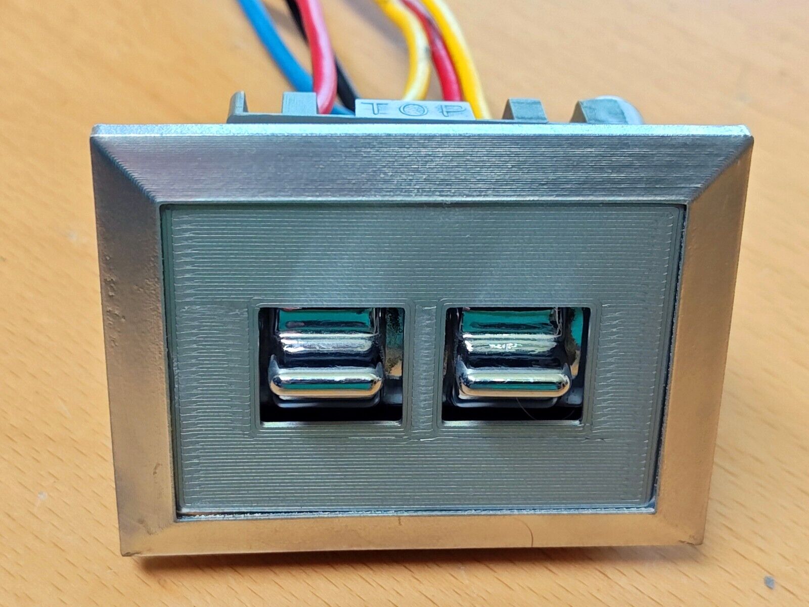 Driver-side dual power window switch bezel for 1980-1986 Ford F-Series trucks and Broncos, featuring a silver outer frame, textured grey insert, and two chrome toggle switches with wiring on top.