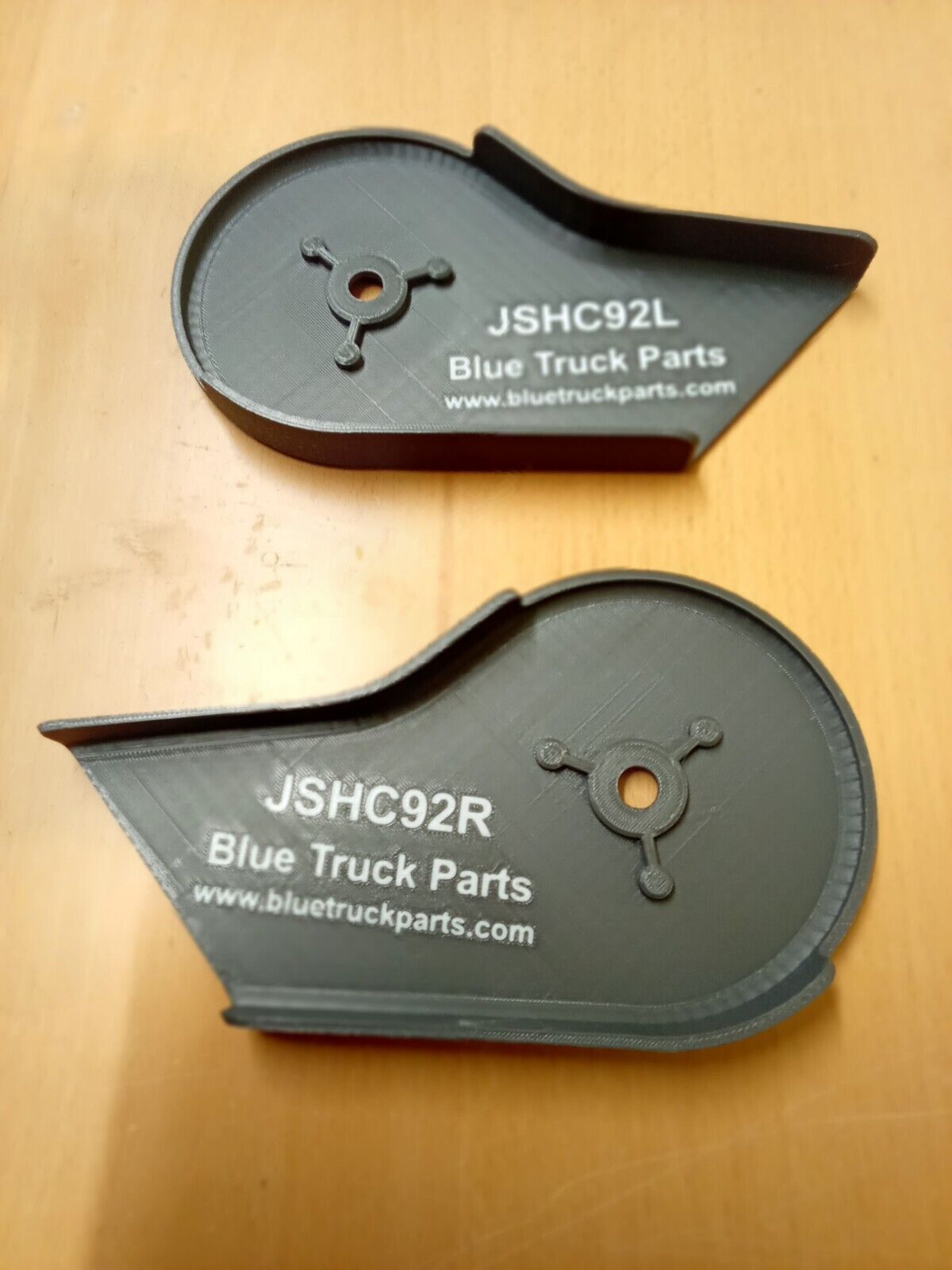 Pair of dark granite gray plastic split seat hinge covers by Blue Truck Parts, labeled JSHC92L and JSHC92R, featuring a textured finish and central mounting holes with reinforced ribs for 92-97 Ford F-Series trucks.