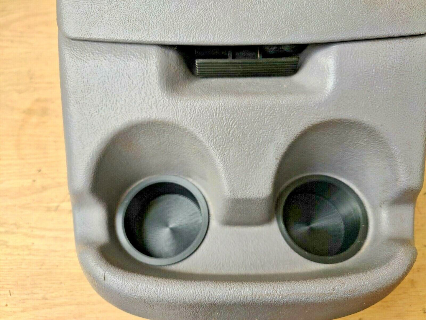 Close-up of two black cup holder inserts installed in a grey textured center console of a 1992-1996 Ford F-Series truck or Bronco.