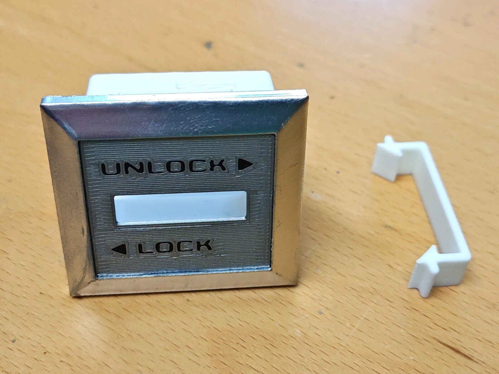 Left power lock bezel for 1980-1986 Ford F-series trucks and Bronco, featuring chrome trim, a grey face with UNLOCK and LOCK text, and a white plastic retainer clip.