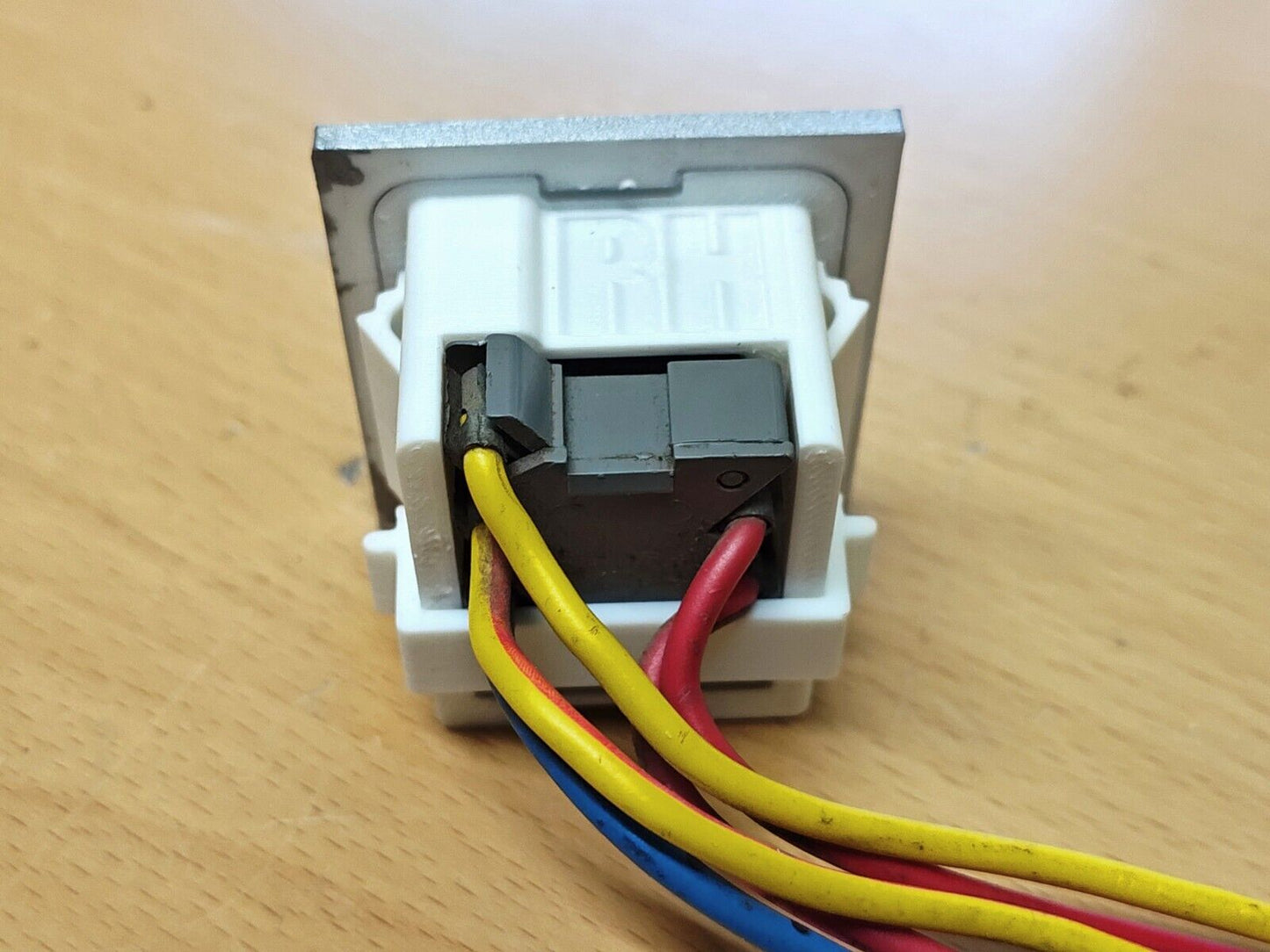 Rear view of a 1980-1986 Ford truck and Bronco right power window bezel showing a grey switch connector with yellow, red, and blue wires plugged into the white polymer housing marked RH.