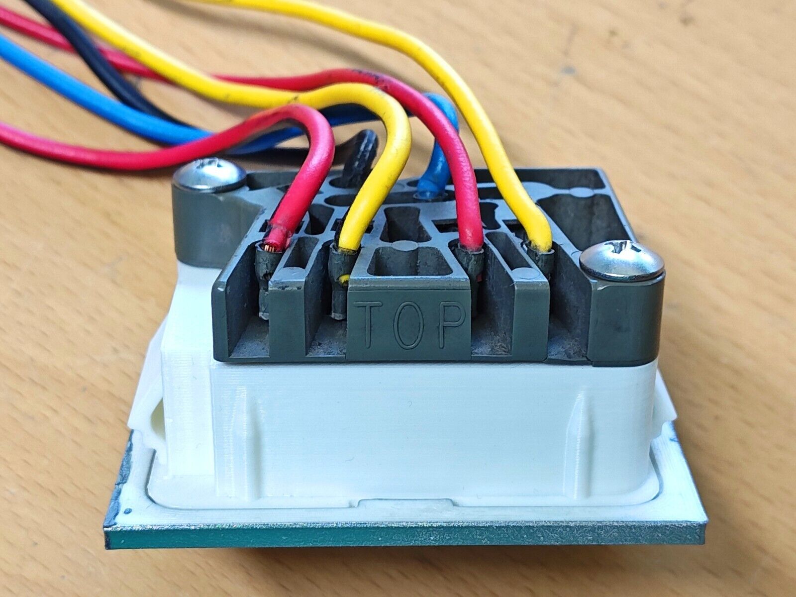 Wiring harness connector with red, yellow, and blue wires secured with screws to a white power window switch housing, featuring 'TOP' embossed on the grey connector body.