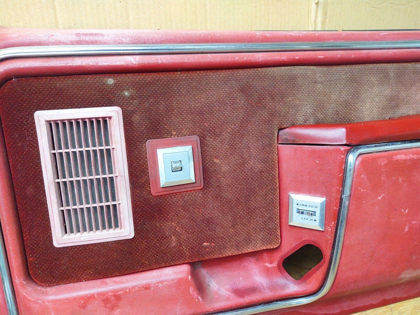 Installed power door lock switch bezel labeled UNLOCK and LOCK on a red passenger-side door panel of a 1980-1986 Ford F-150, F-250, F-350, or Bronco.