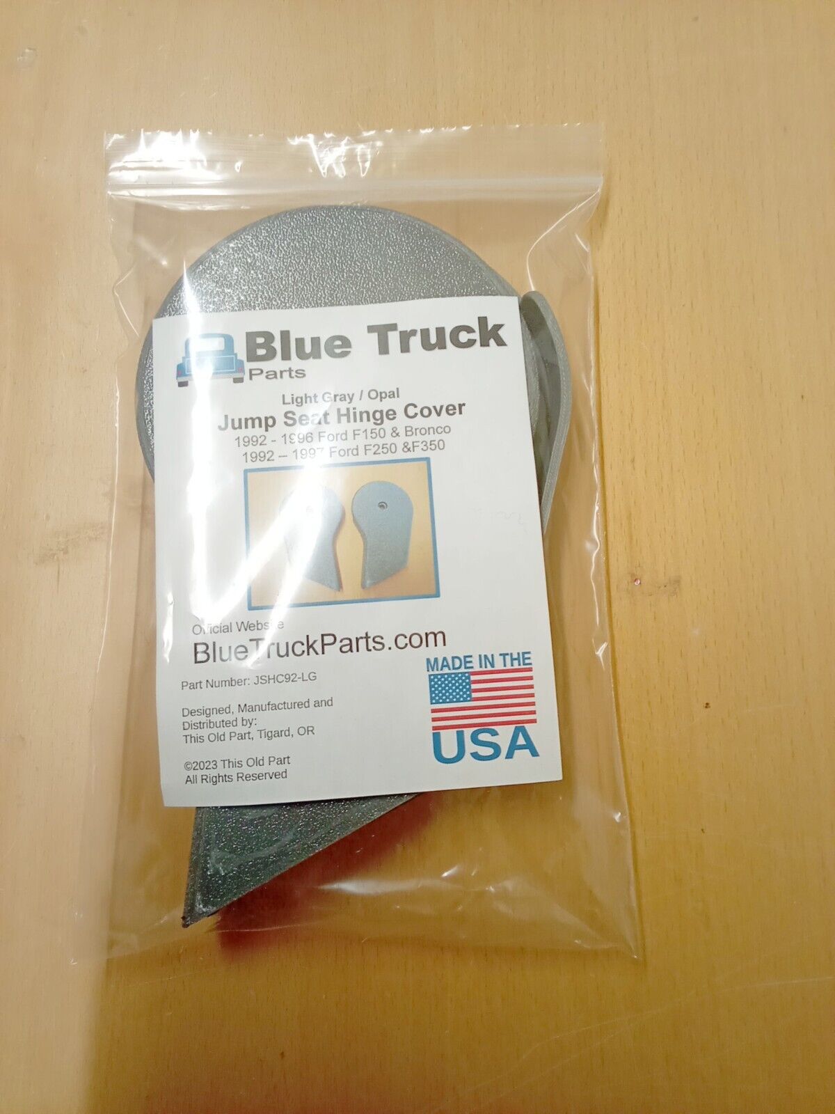 Packaged Blue Truck Parts light gray jump seat hinge covers in a clear plastic bag with an insert label showing compatibility for 1992 to 1997 Ford F150, F250, and F350 trucks.